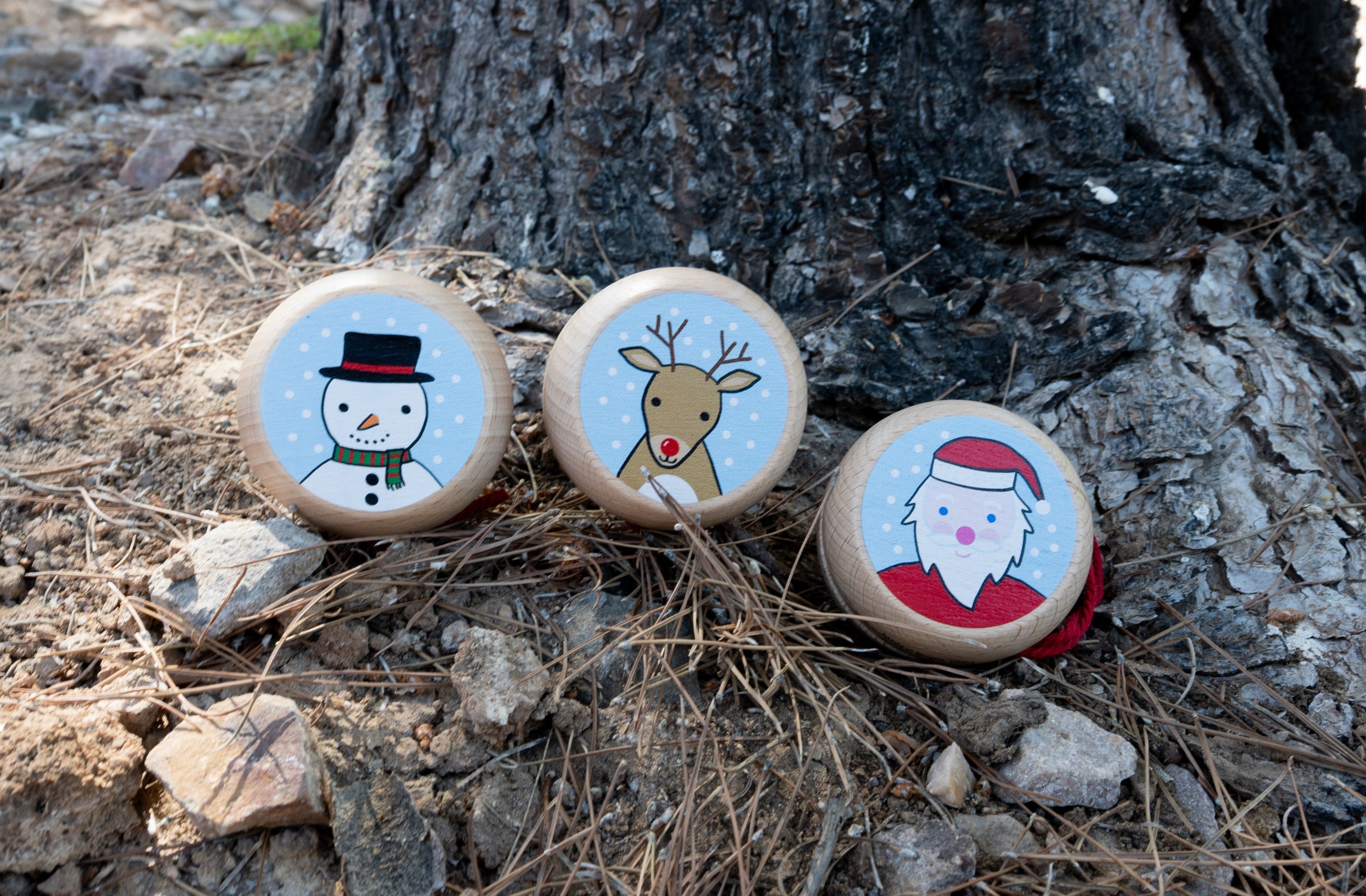 Three round wooden Christmas yo-yos with printed holiday illustrations of a reindeer, Santa Claus, and a snowman on a white background.